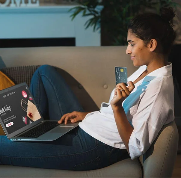 Female user holding payment card while browsing IPTV content on laptop for movies and live TV