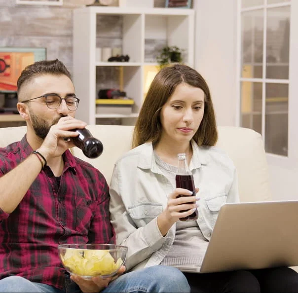 Couple sitting in front of a laptop with soft drinks, enjoying IPTV streaming or online content together